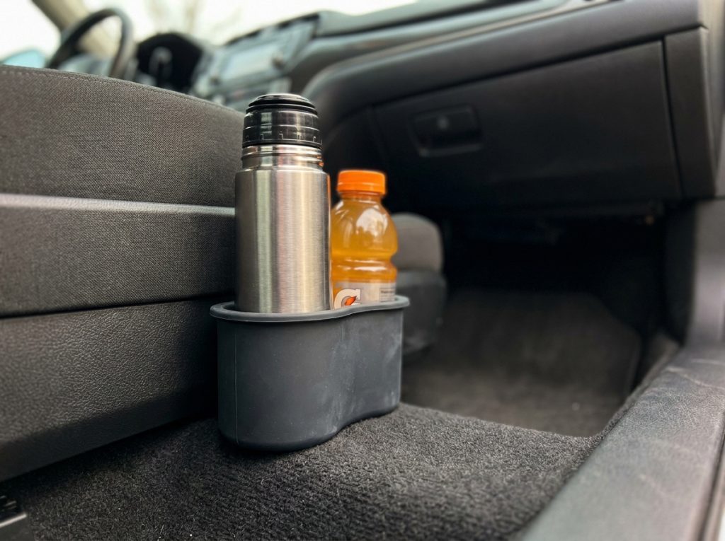 Gros plan d'un range-gobelet en silicone maintenant un thermos et une bouteille de jus dans le plancher passager d'une voiture